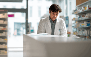 Pharmacist reviewing documents at a modern pharmacy counter, symbolizing financing that supports independent pharmacy growth.