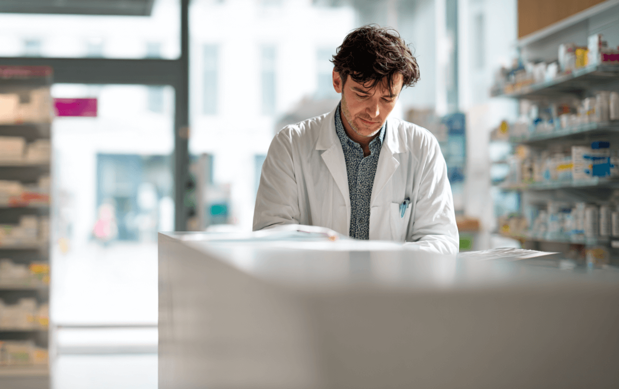 Pharmacist reviewing documents at a modern pharmacy counter, symbolizing financing that supports independent pharmacy growth.