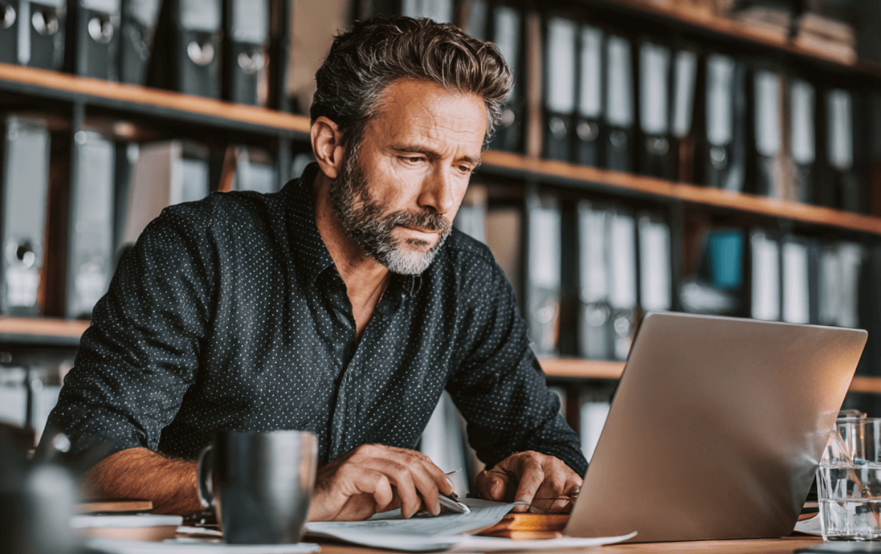 Business owner reviewing ACH loan approval documents on a laptop at a small office